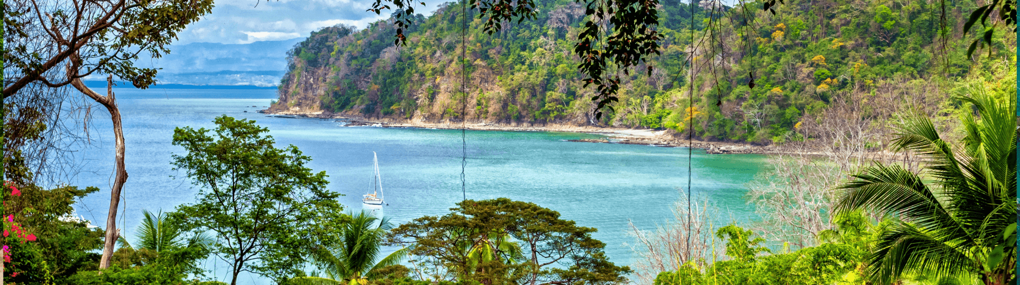 Tropical bay in Costa Rica with turquoise water, forested coastline and a sailboat
