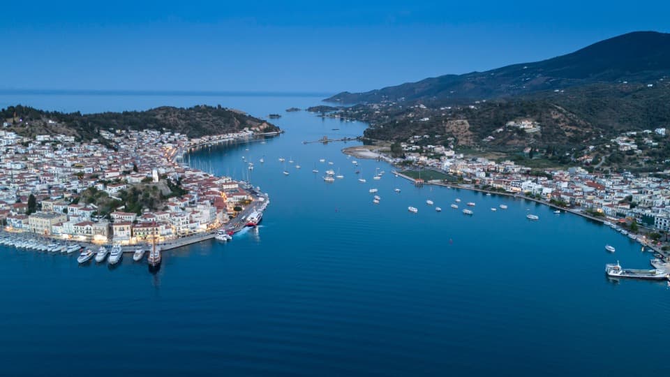 Aerial view of a Greek coastal town with harbor, boats, and a calm bay