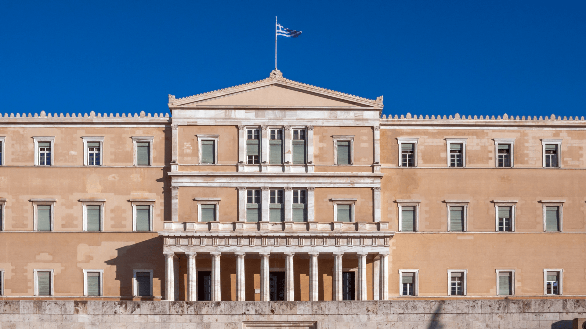 Greek Parliament building in Athens with flag under a clear blue sky