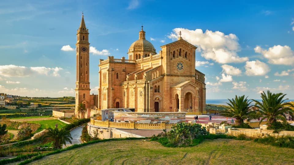 The majestic Ta' Pinu Basilica on Gozo, surrounded by lush greenery under a blue sky – a symbol of Maltese culture and faith.