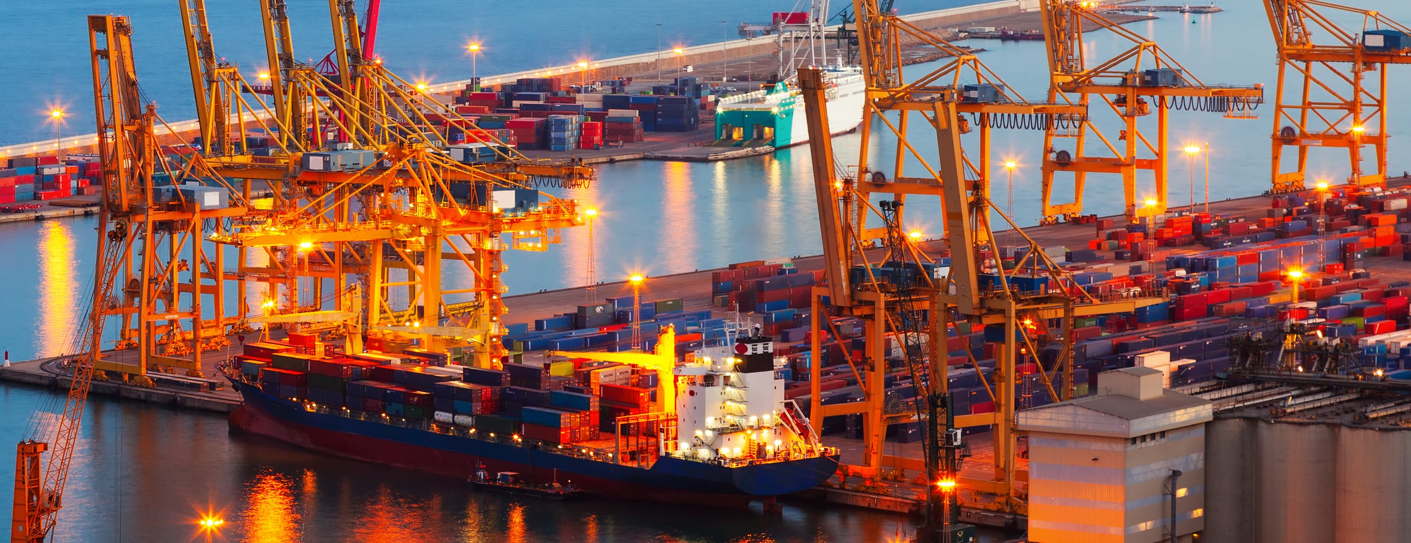 Night view of container port with ship, cranes, and containers; customs clearance in sea freight.