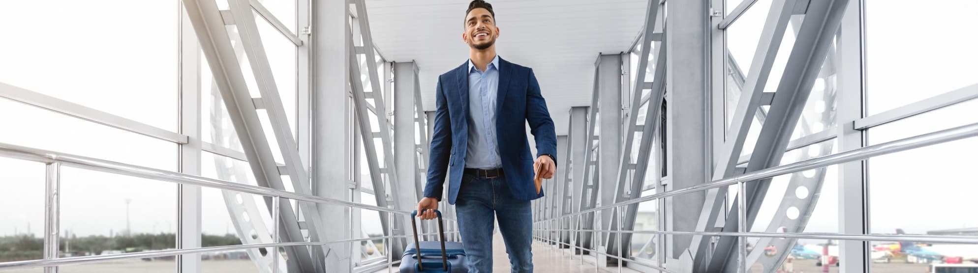 A smiling expat in business attire pulls a rolling suitcase through a modern airport terminal on the way to an international assignment.