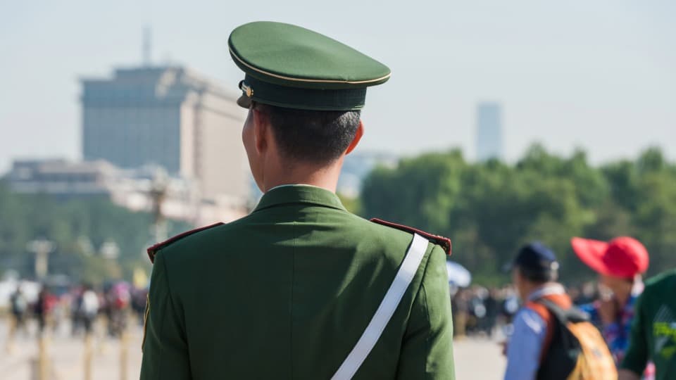 A uniformed guard in a green military uniform looking out over a crowd in a major Chinese city – Safety when emigrating to China