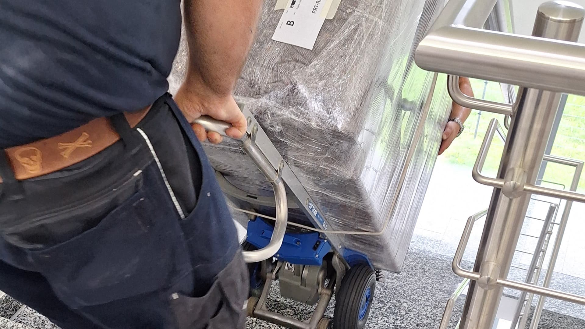 Worker uses a stair climber to move a wrapped piece of furniture safely up the stairs.