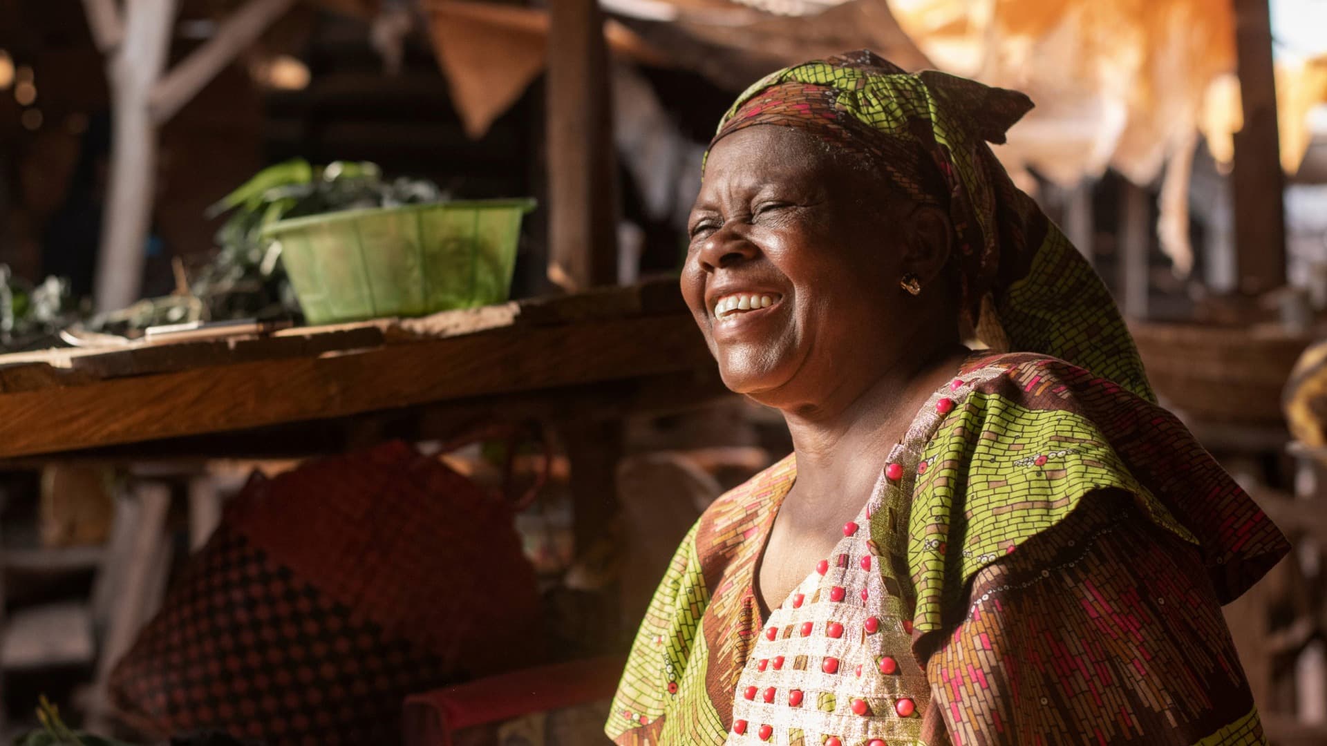 Portrait of a woman in colorful clothing in front of a simple hut