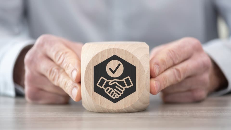A wooden cube with a handshake symbol representing award-winning reliability in B2B projects with DACHSER & KOLB.