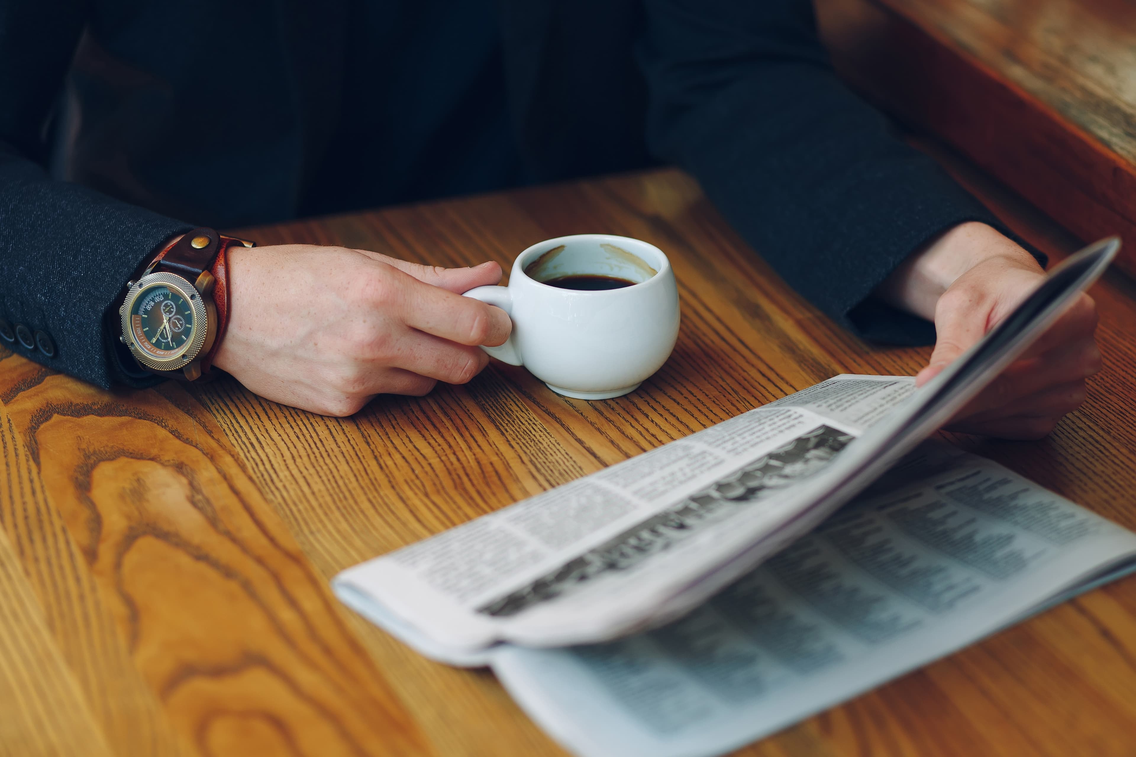 Person reading a newspaper and drinking coffee – moment of staying informed and reflecting on current news.