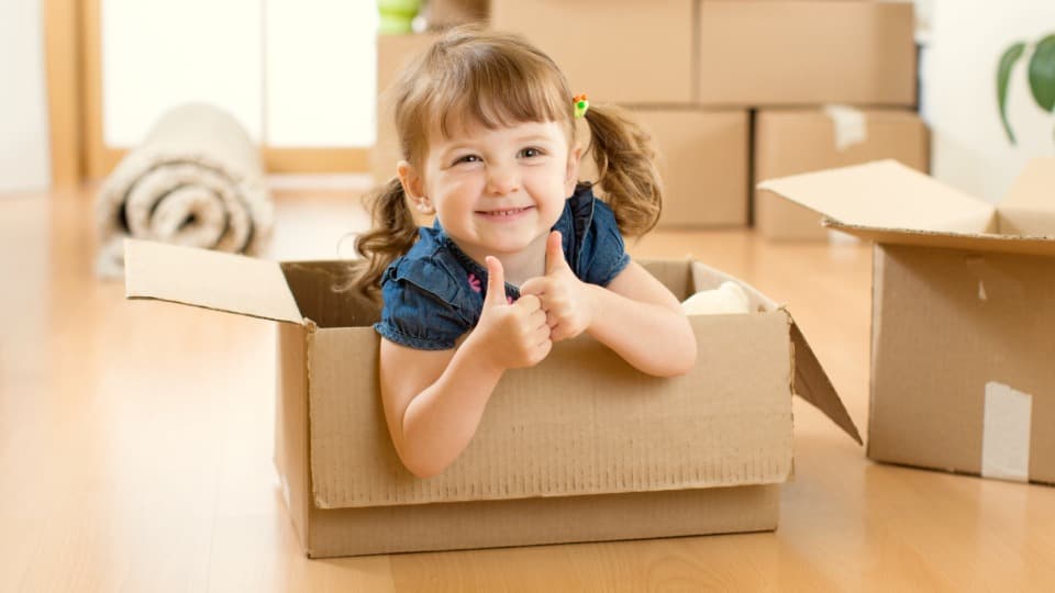 A happy little girl giving a double thumbs up from inside a moving box during a relaxed international family relocation with DACHSER & KOLB.