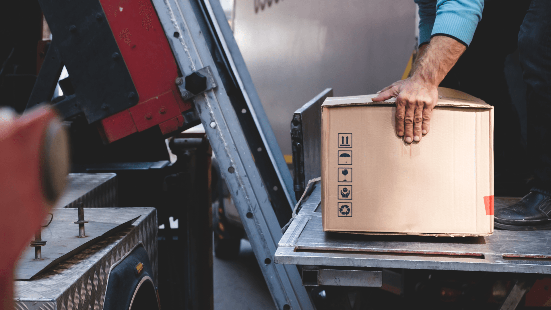 Worker places moving box on external lift platform at a truck.
