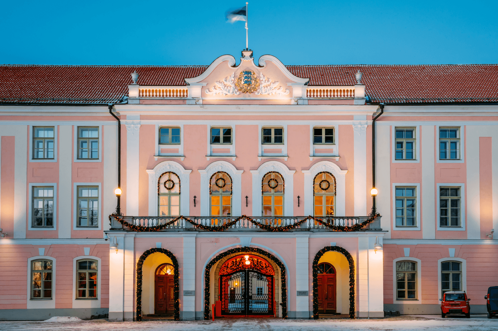 Historic building in Estonia with Estonian flag, pink facade and illuminated entrance