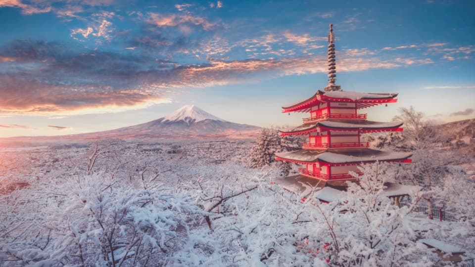 Snow-covered pagoda with view of Mount Fuji at sunset in Japan