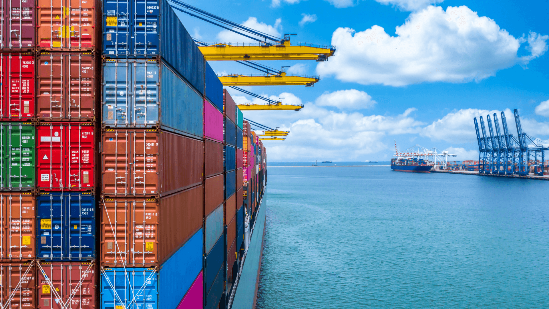 A large container ship loaded with colorful containers of various sizes in the port under a blue sky.