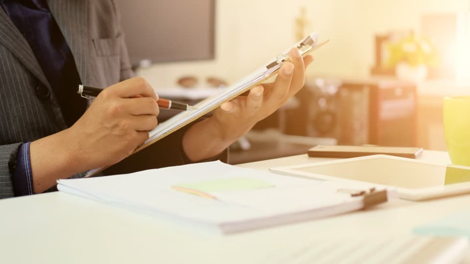 A business professional reviews and documents service records on a clipboard in the office – symbol image for standardized invoicing and audit reliability in procurement.