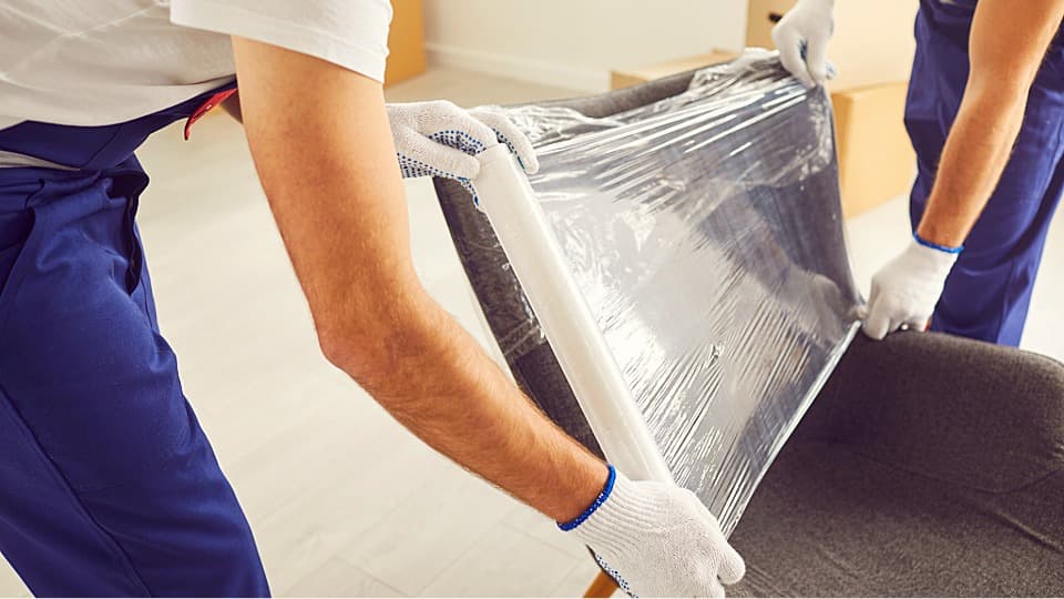 Two movers carefully wrapping an office chair in stretch film for safe temporary storage.