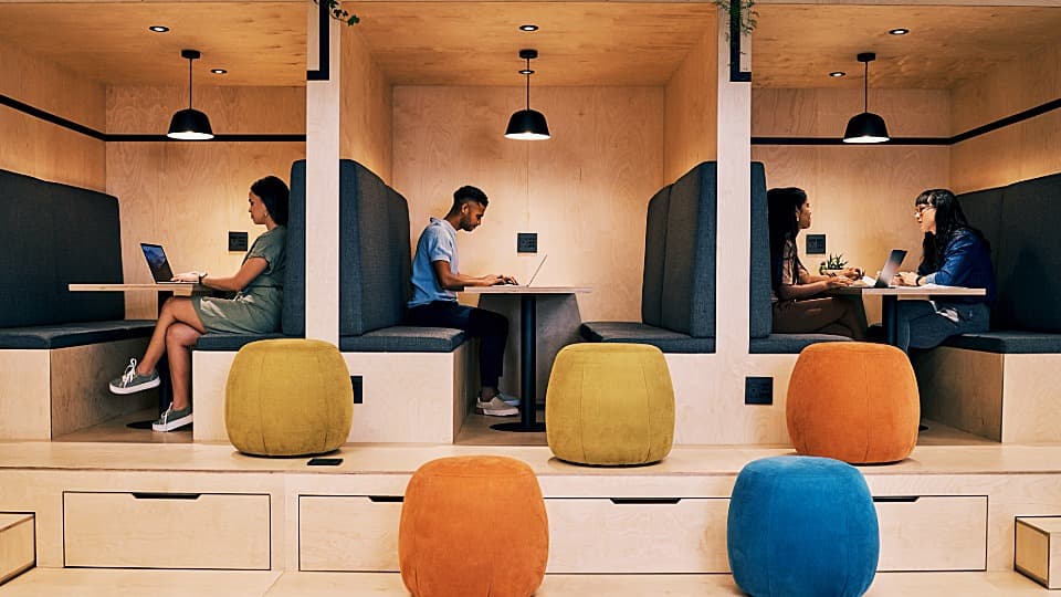 Employees working with laptops in modern seating booths in a flexible co-working office with a New Work design.