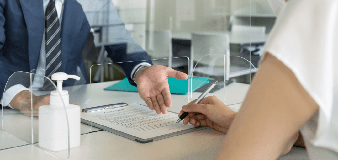 Person signing deregistration form after moving, at a public office counter with a plexiglass screen.