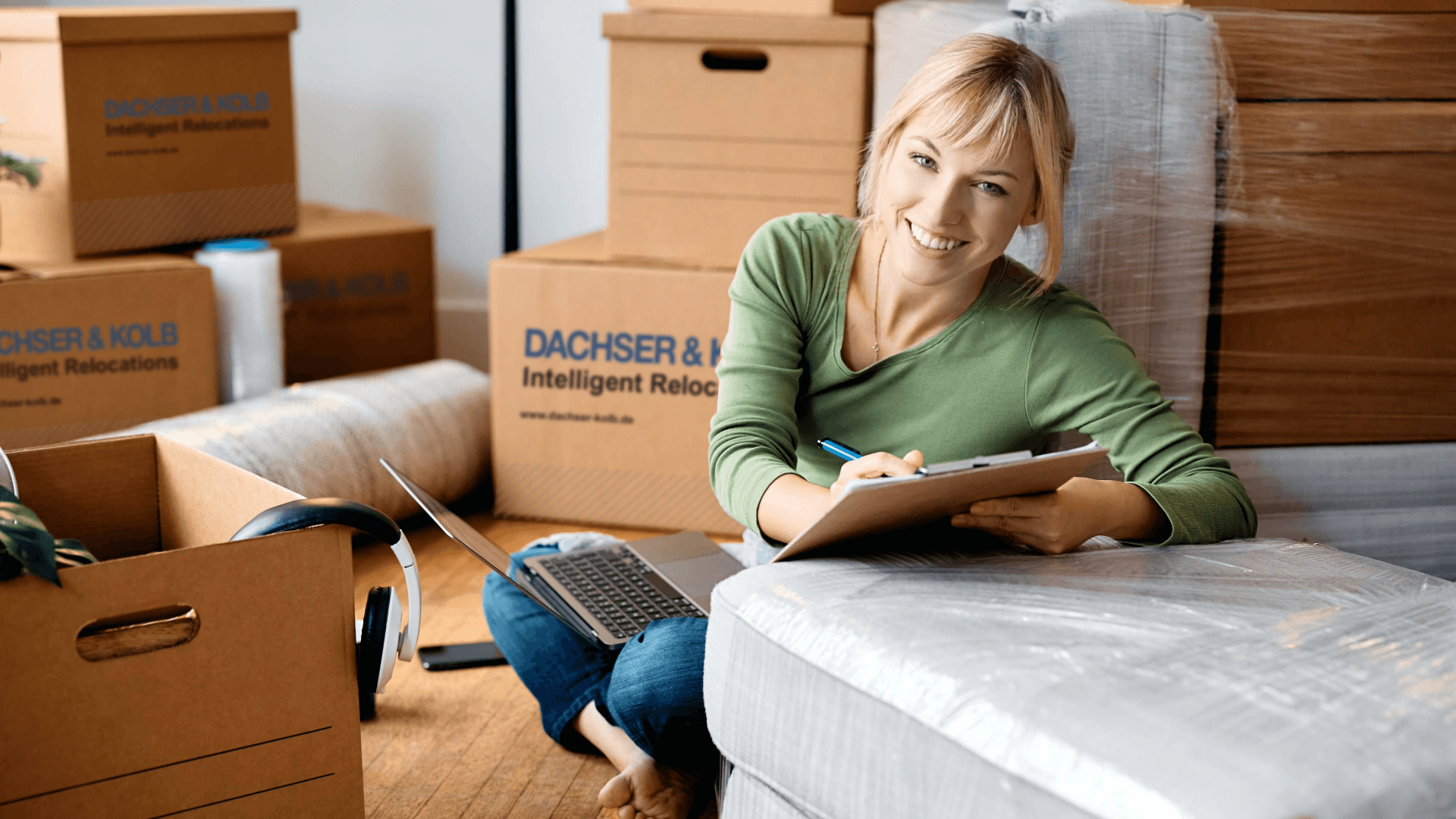 Woman planning her move with clipboard and laptop among moving boxes