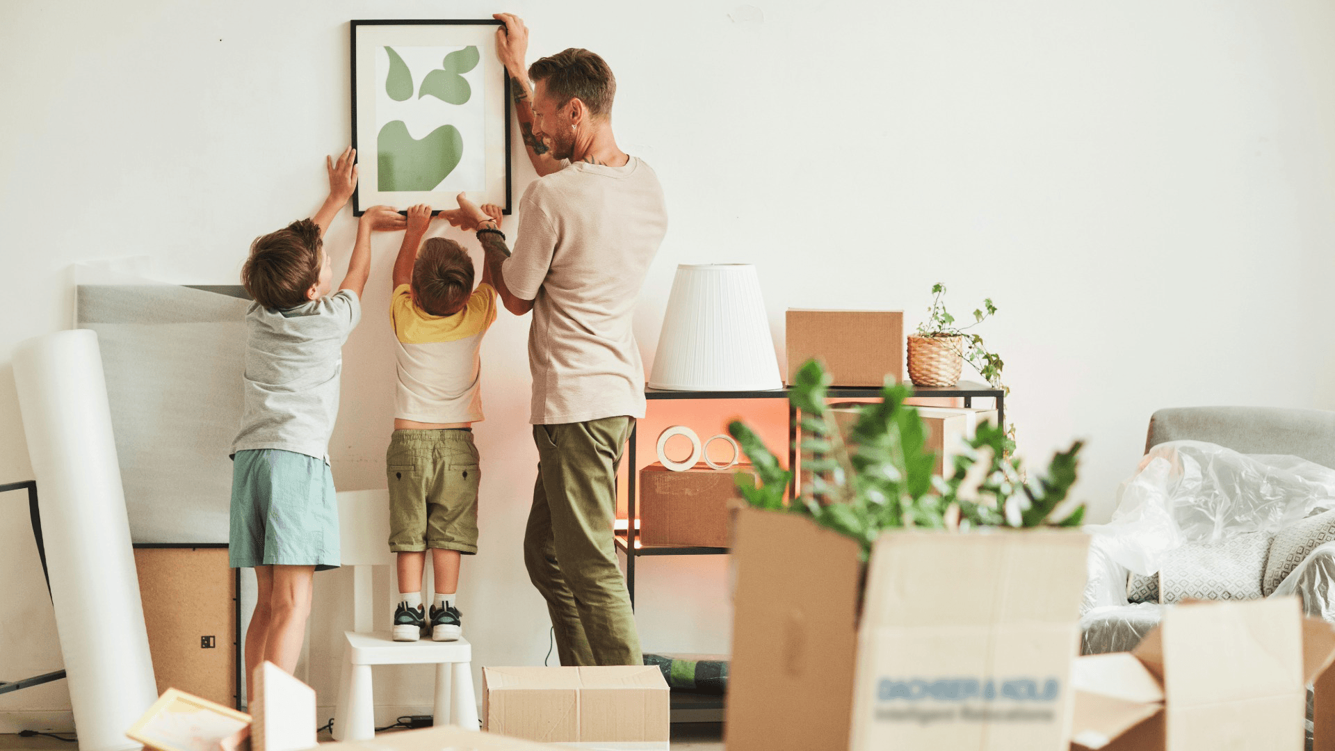 Family hanging picture in new home with moving boxes, moving on a budget
