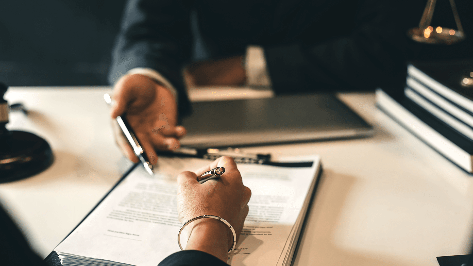 One person signs a contract while another offers a pen. Symbolizes contract finalization with Incoterms.