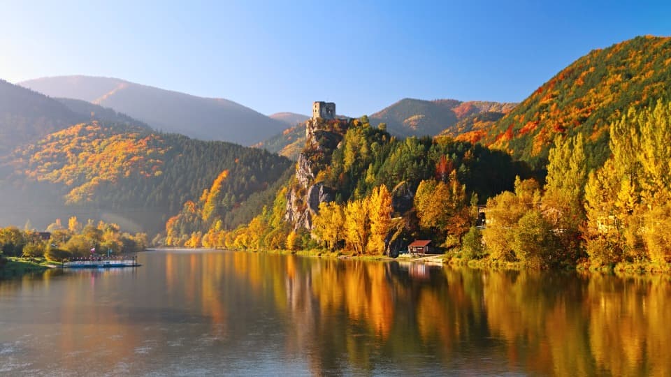 A landscape in Slovakia featuring bodies of water, forests, and mountains, with the ruins of a castle