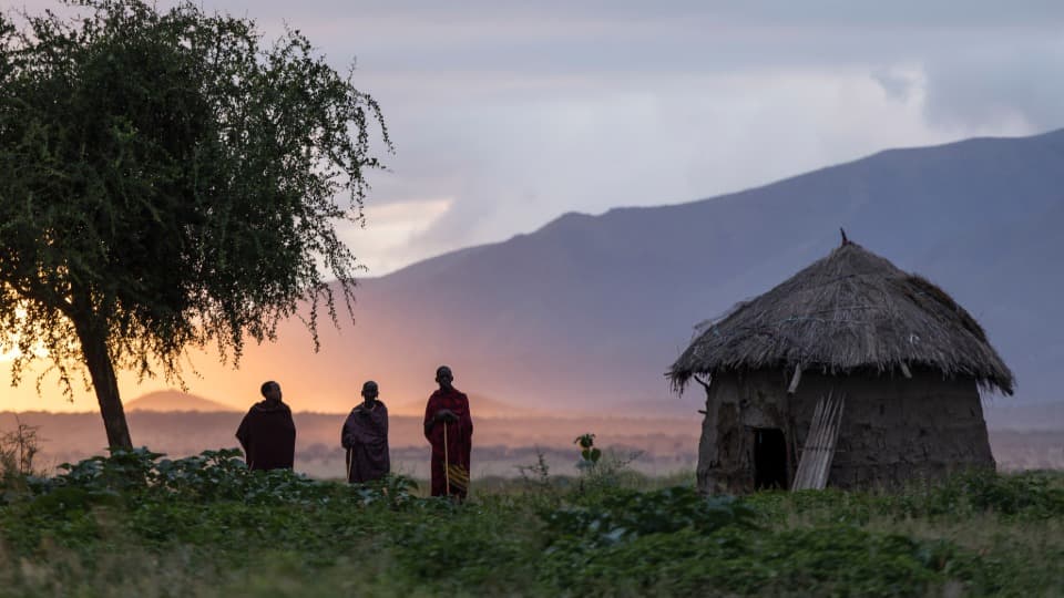 Three people are standing next to a hut in Tanzania at sunrise
