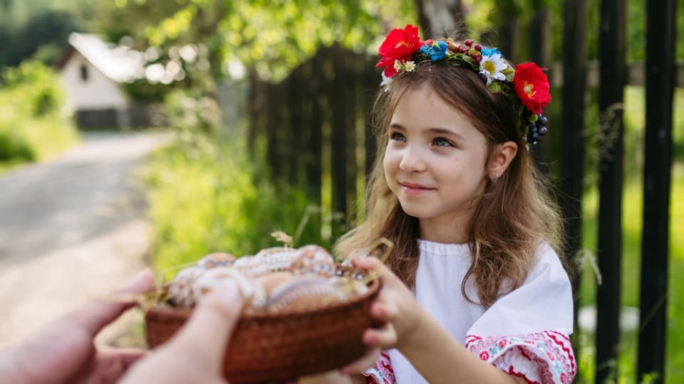 A little girl in traditional Slovakian folk costume is holding a basket of Easter eggs