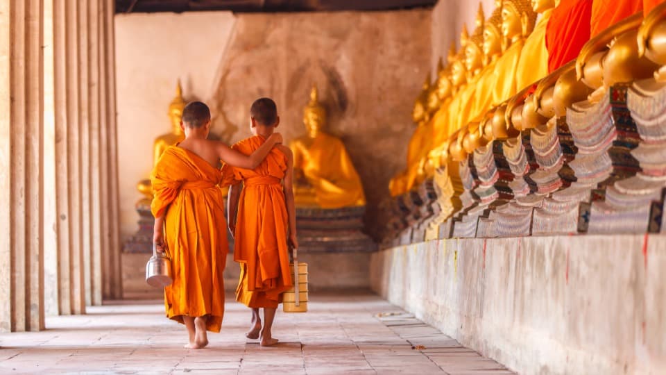 Two Buddhist monks walk arm in arm through a temple in Thailand