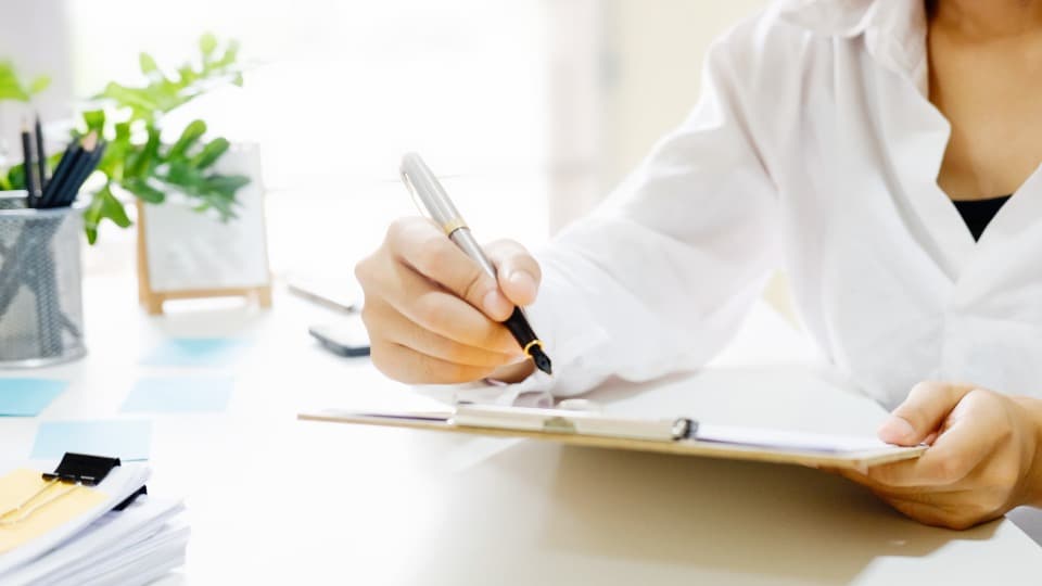 Compliance in the B2B process at DACHSER & KOLB – A person signs documents on a clipboard with a fountain pen at a desk.