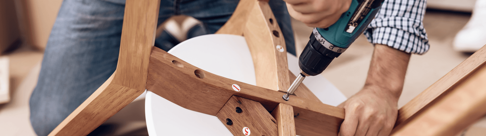 Furniture assembly made easy: person using cordless screwdriver to build wooden chair with visible instructions