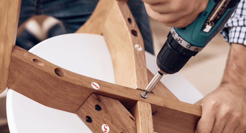 Furniture assembly made easy: person using cordless screwdriver to build wooden chair with visible instructions