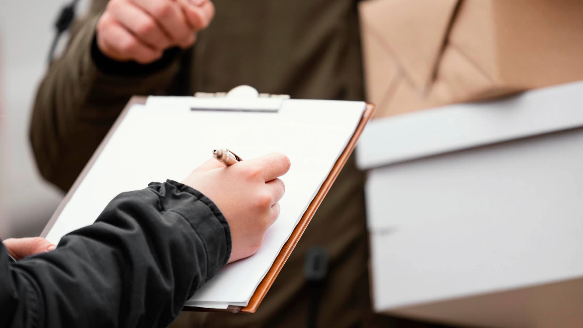 A person signing on a clipboard while a delivery person holds packages. Symbolizes the handover of goods.