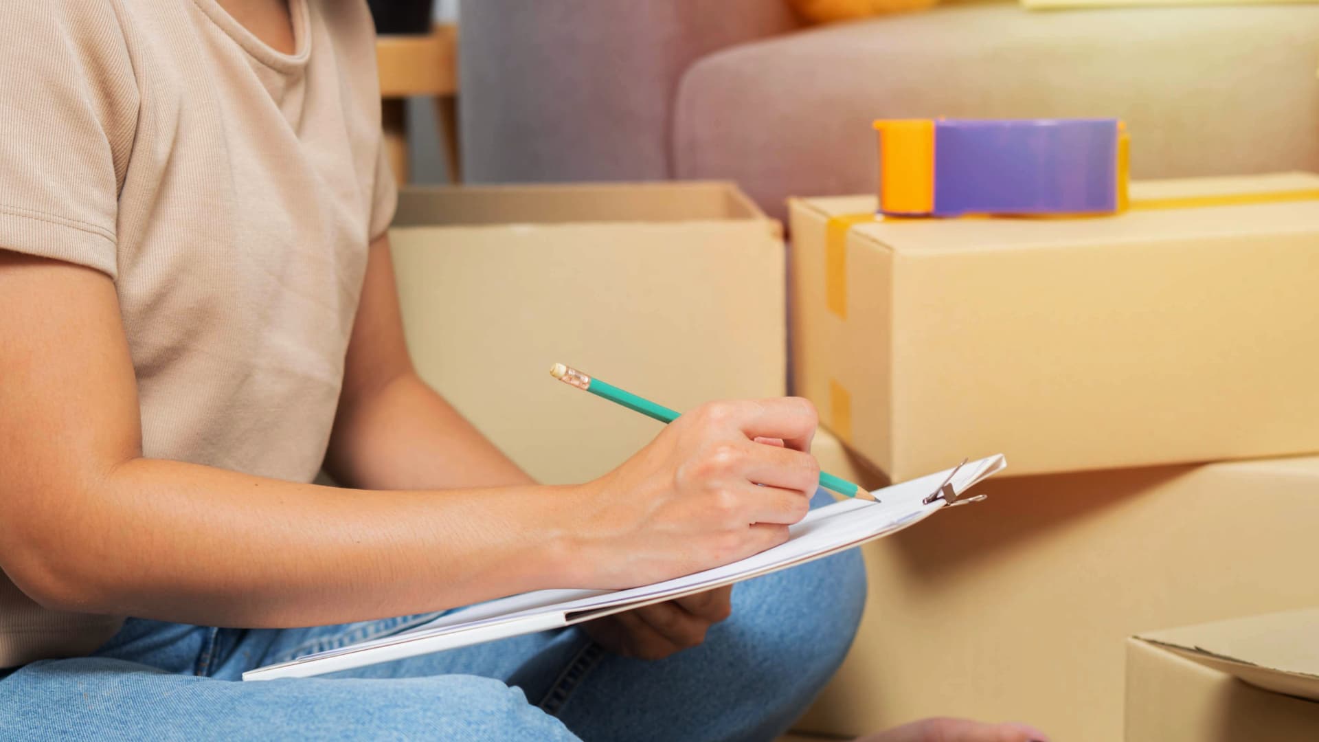 Person sitting among moving boxes, making an inventory list, typical for a "Packed by Owner" (PBO) move.