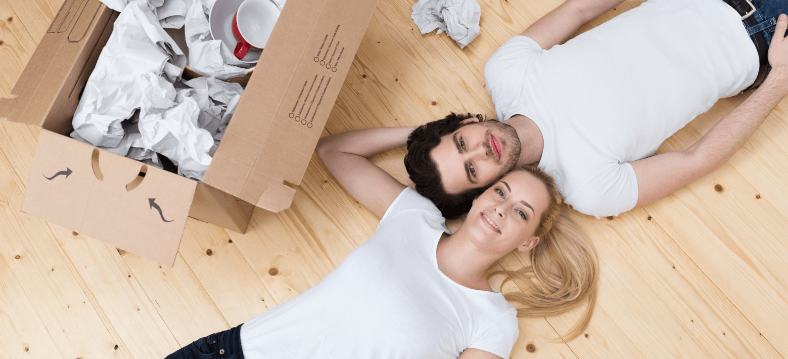 Happy couple lies relaxed next to unpacked box. Priorities when moving: Unpacking essentials first, taking time.