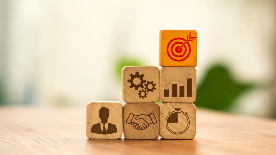 Stacked wooden blocks arranged like steps with business symbols representing structured project workflows, scheduling, and coordination in professional facilities logistics.