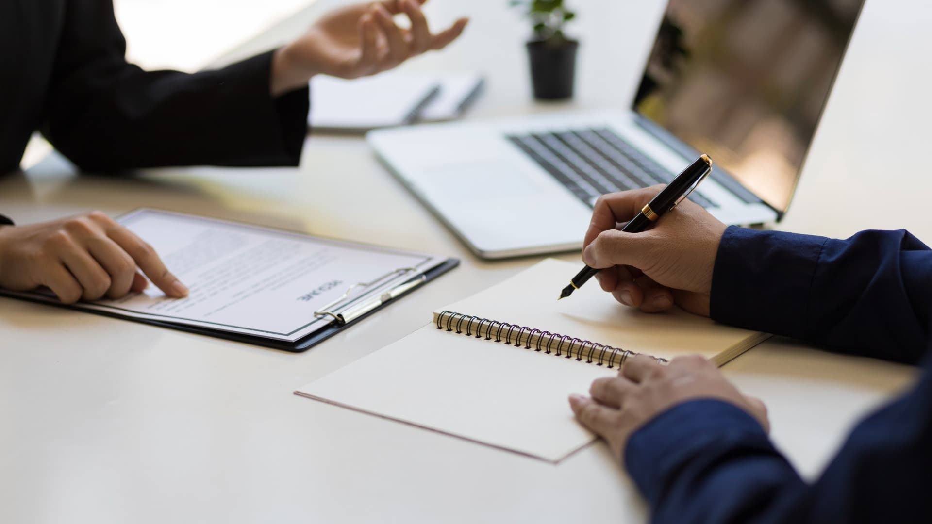 Two people at a desk: one takes notes, the other points at documents. Symbolizing relocation service for private individuals.