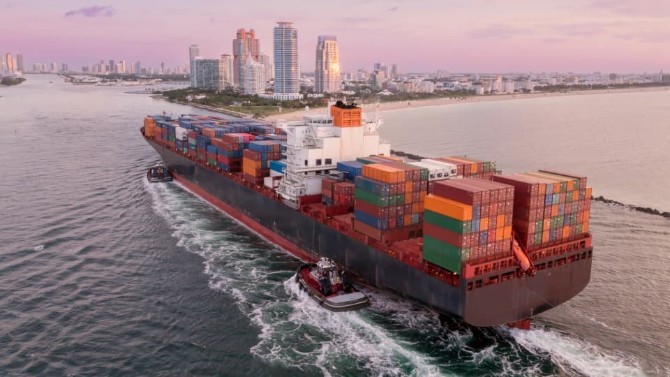 Ein großes Containerschiff von DACHSER & KOLB auf dem Seeweg in die USA transportiert Umzugscontainer über den Ozean vor einer Skyline für den sicheren Überseeumzug.