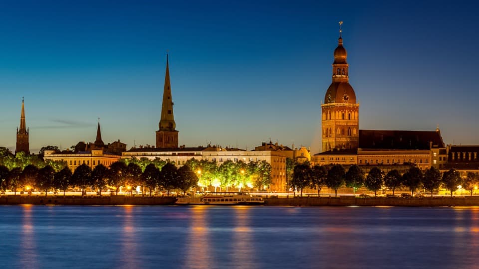 The illuminated silhouette of Riga’s Old Town at night – a symbol of stability and security in Latvia, a popular destination for immigrants.