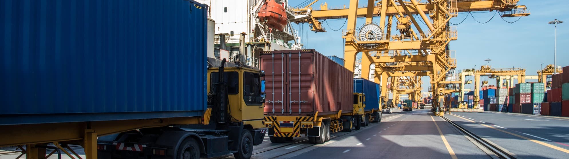 Trucks carrying containers at a container terminal, port cranes in the background – TEU-based container logistics