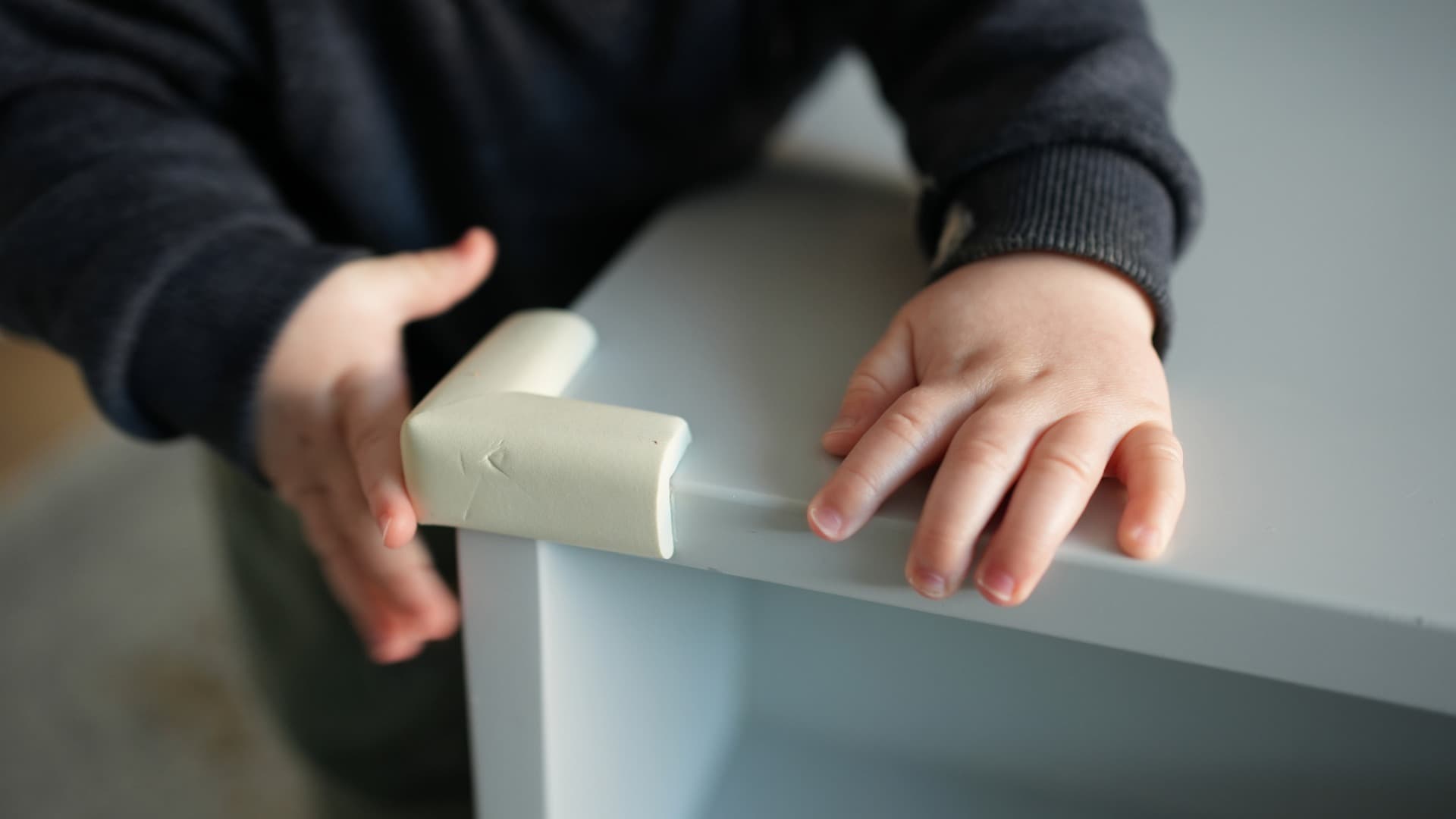 A Person adds a corner guard (edge protection) to a table corner to prevent bumps and injuries