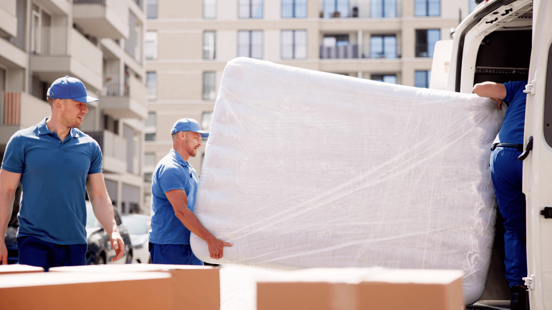 Moving Hamburg Munich: Movers carrying mattress into moving van. Accessible image.