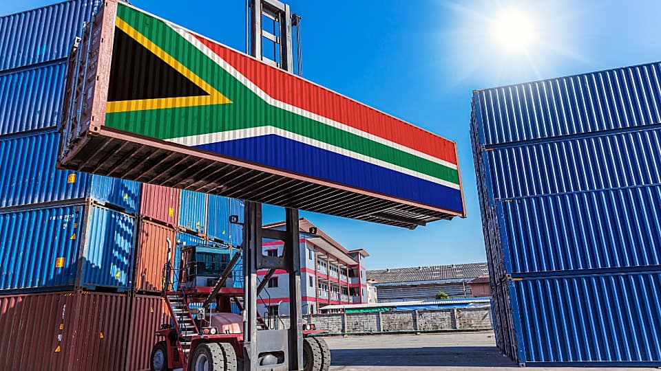 Ein Containerstapler verlädt einen Übersee-Container mit südafrikanischer Flagge im Hafen für den Container-Umzug nach Südafrika mit DACHSER & KOLB.