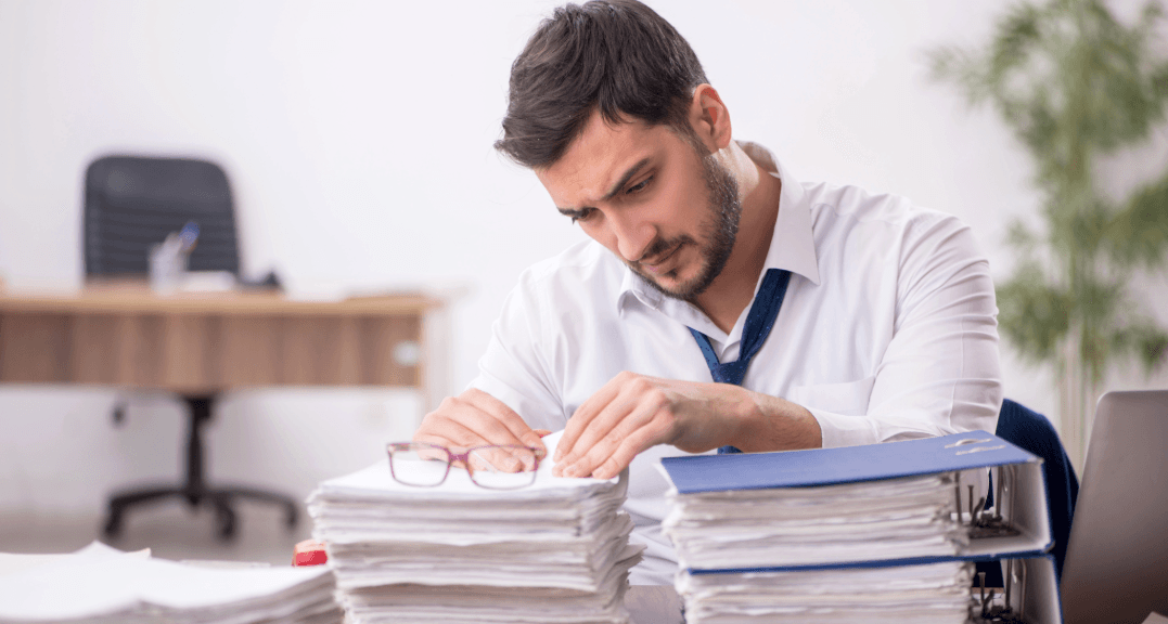 Clerk reviewing documents for deregistering after moving, at a crowded office desk.