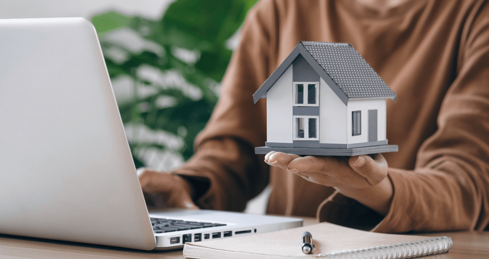 Woman checks insurance after moving online while holding a model house symbolizing property protection.